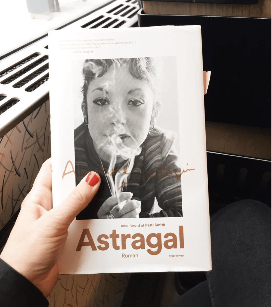 Et billede af bogen Astragal taget i et tog. På forsiden er et billede af forfatteren Albertine og der står at Patti Smith har skrevet forordet til bogen